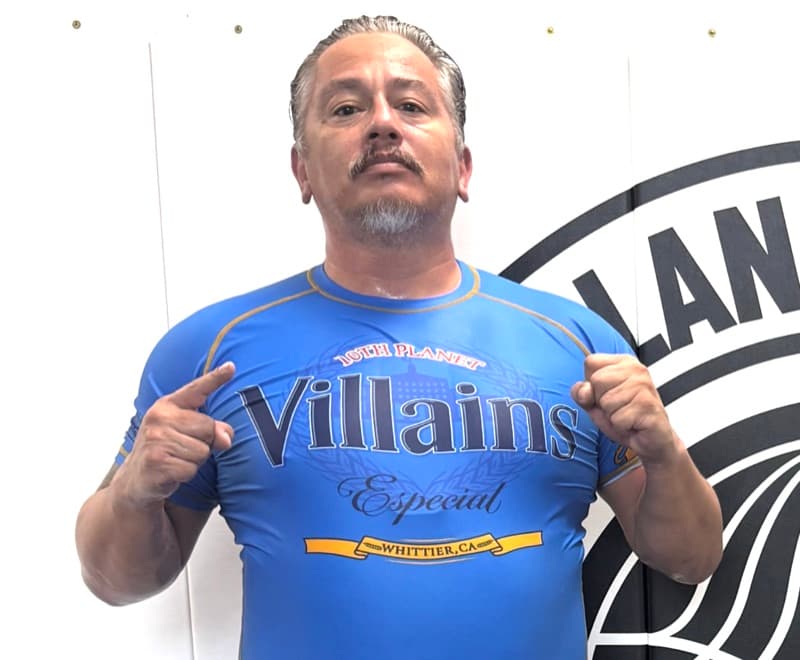 Fred in a Villains rash guard at his gym, pointing at the logo