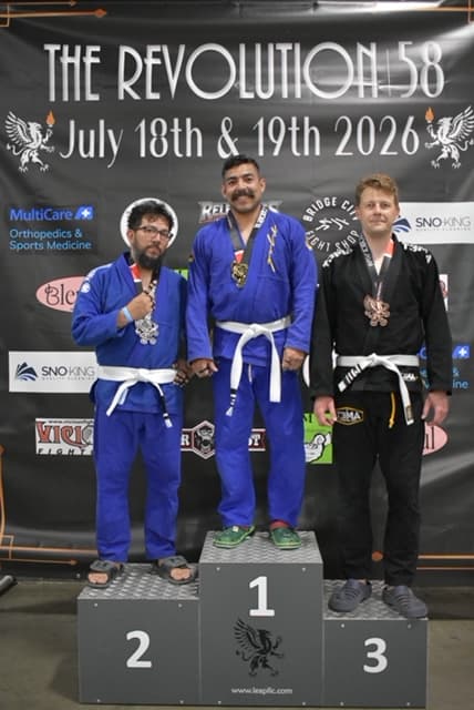 Josue on the second-place step of the podium at The Revolution 58 BJJ competition, medal around his neck