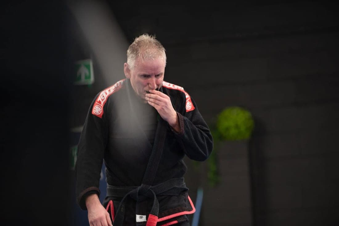 Noel in his black gi and black belt on the mats, putting in his mouthguard